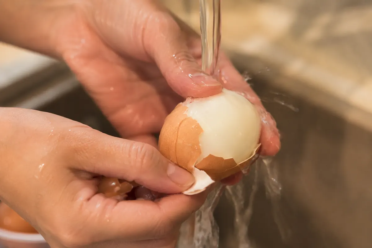 Hands peeling a hard boiled egg under running water with shell coming off cleanly