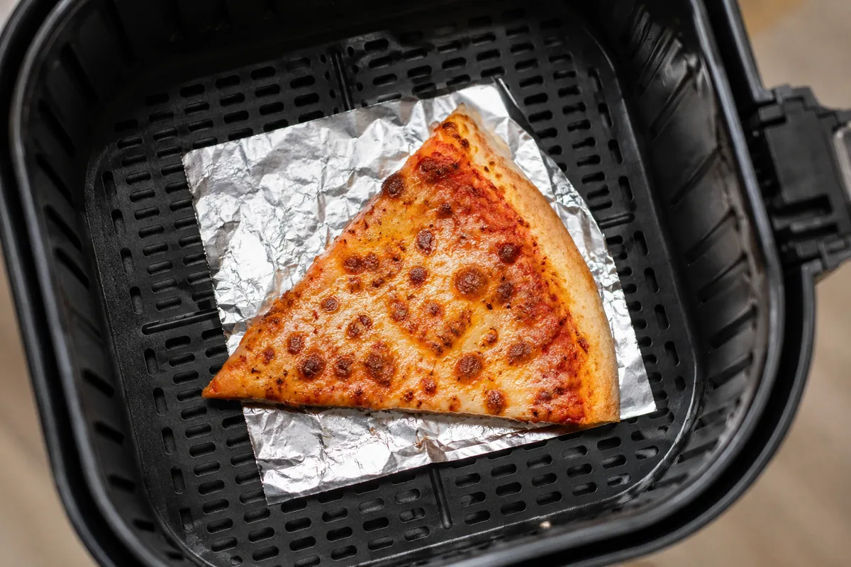 Pizza slice on a small foil square in an air fryer basket with open airflow around it