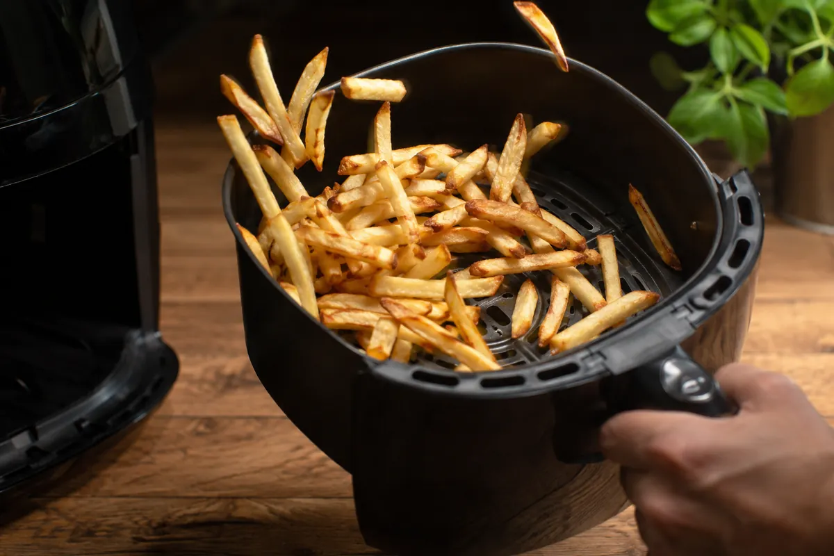 Shaking the fries basket mid-cook Hand shaking an air fryer basket of partially cooked fries
